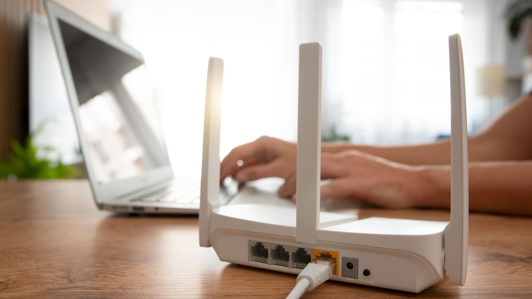 Router WiFi doméstico junto a un ordenador portátil para comprobar dispositivos conectados y detectar intrusos.