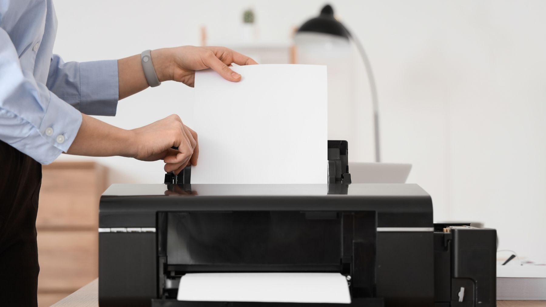 Persona colocando una hoja en una impresora, ejemplo de impresión que puede incluir puntos amarillos ocultos de identificación.