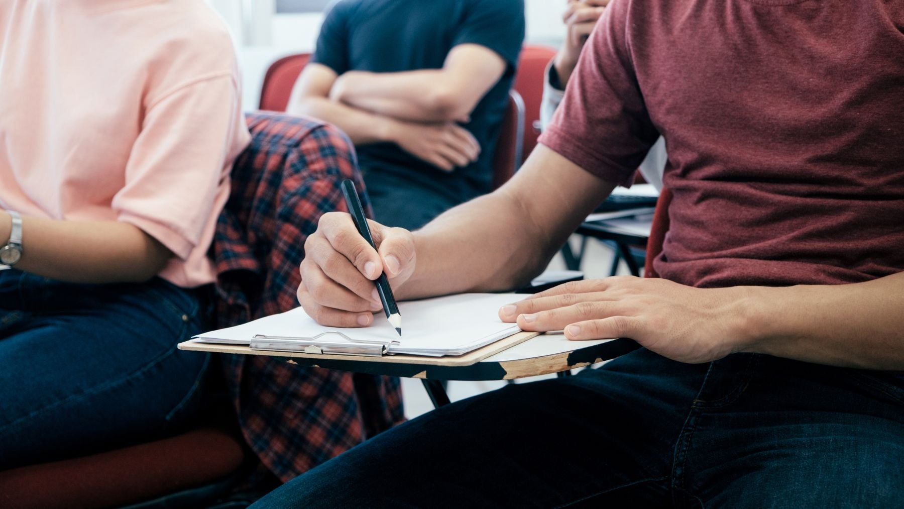 Estudiantes universitarios en clase escribiendo apuntes en un aula durante un examen.