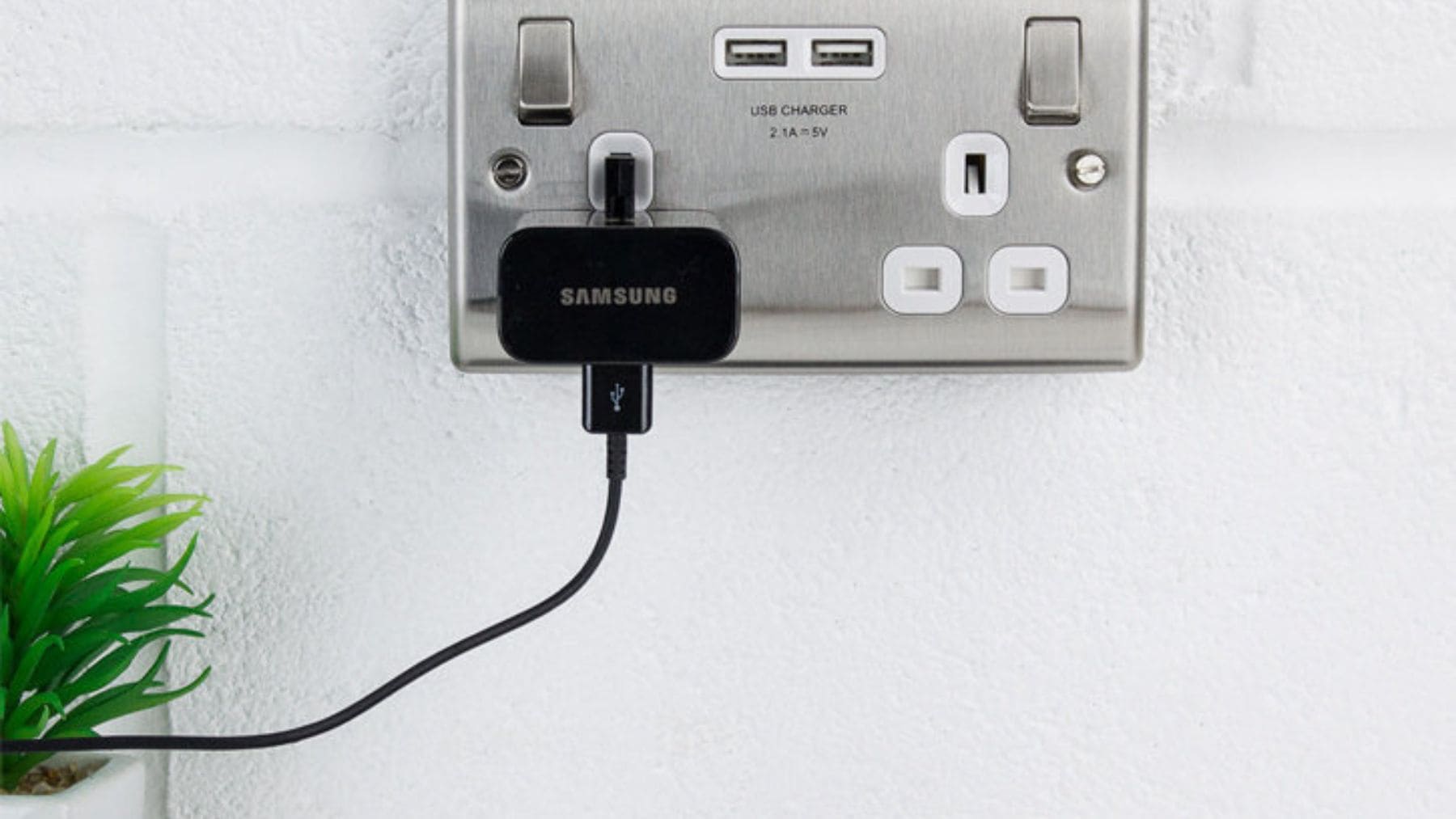 Cargador Samsung enchufado a la pared con un móvil conectado mediante cable USB para cargar la batería.