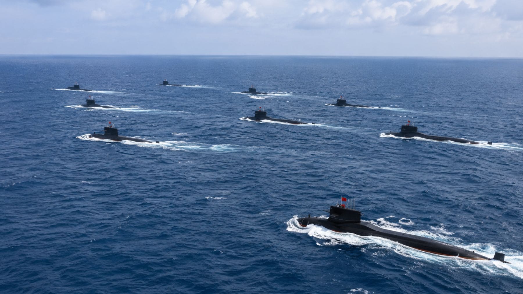 Formación de submarinos nucleares chinos Tipo 094A y Tipo 093B navegando en el océano durante una exhibición naval.