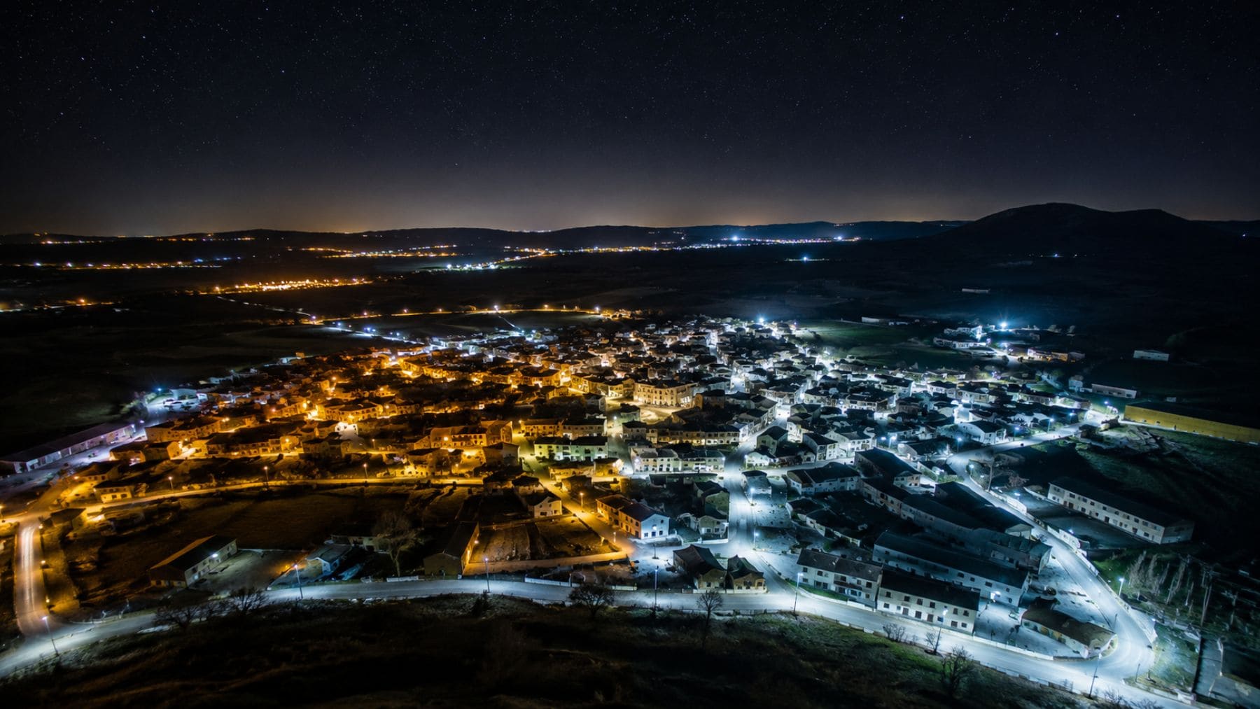 Vista aérea nocturna de un pueblo español con iluminación LED blanca y amarilla que refleja el aumento de la contaminación lumínica detectada por el satélite SDGSAT-1.