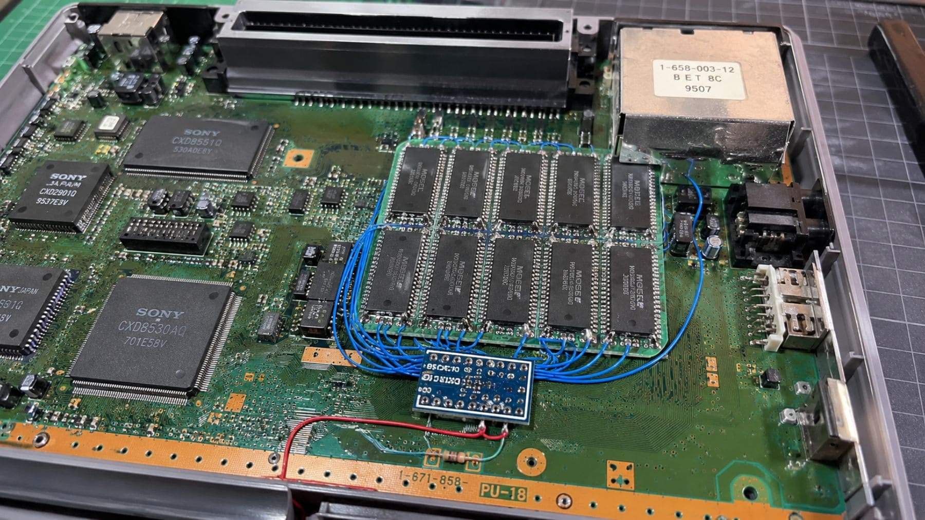 Interior de una PlayStation original con el mod que amplía la memoria RAM de 2 MB a 16 MB mediante nuevos chips soldados.