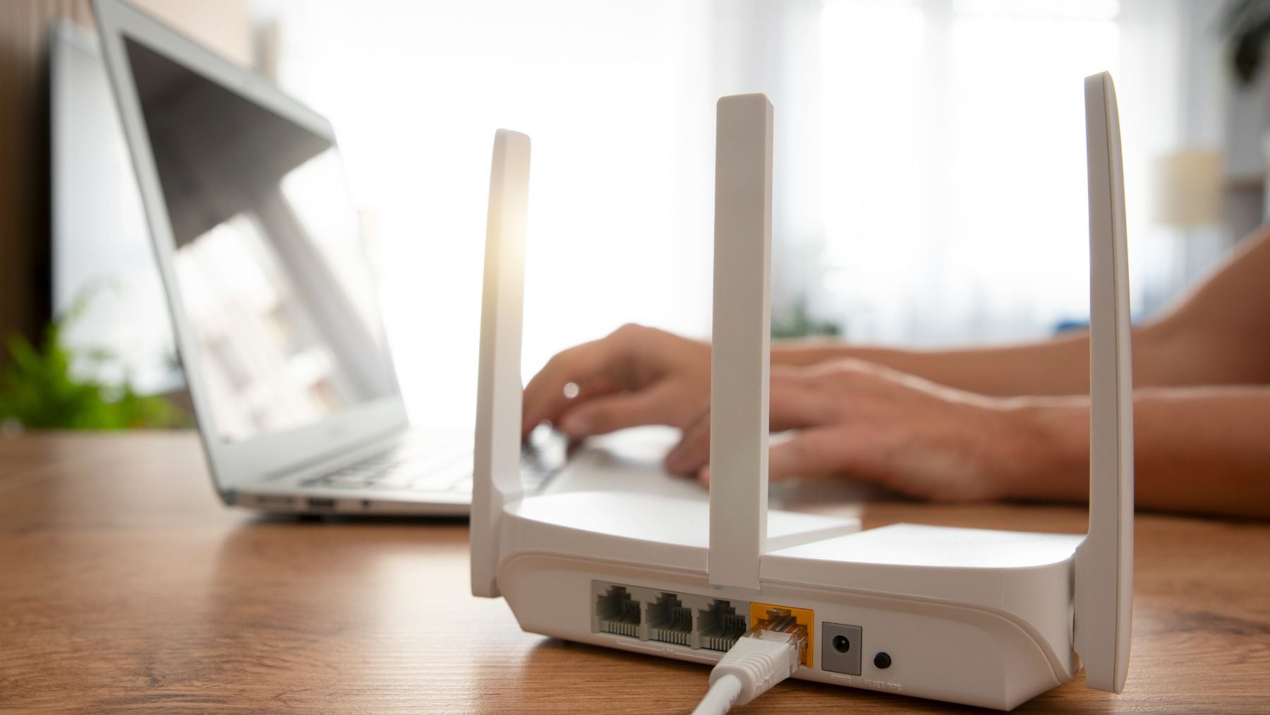 Router WiFi instalado sobre una mesa junto a un ordenador portátil en una vivienda para ilustrar cómo su ubicación afecta a la cobertura de Internet.